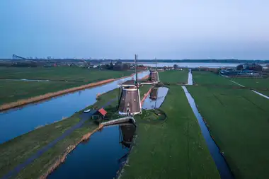 Vista aérea de pólderes verdes con canales rectos y molinos de viento al atardecer en el campo holandés