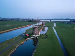 Vista aérea de pólderes verdes con canales rectos y molinos de viento al atardecer en el campo holandés