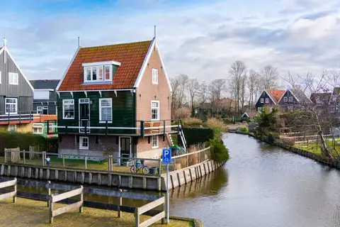 Casa de madera verde con tejado rojo junto a un canal de Marken, con otras casas tradicionales al fondo