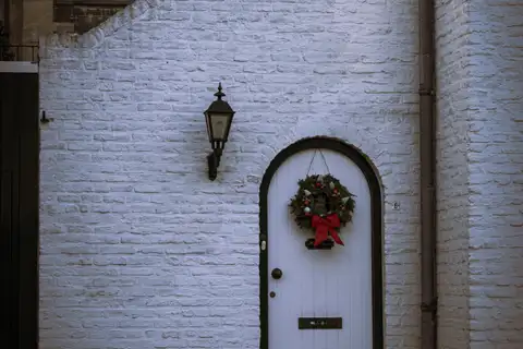 Fachada encalada de ladrillo blanco con una puerta en arco y una corona navideña en el casco antiguo de Thorn