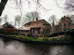 Canal de Giethoorn con casas de ladrillo y tejados de junco, jardines cuidados y un puente de madera