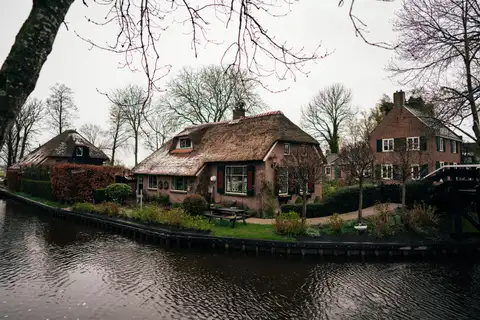 Canal de Giethoorn con casas de ladrillo y tejados de junco, jardines cuidados y un puente de madera