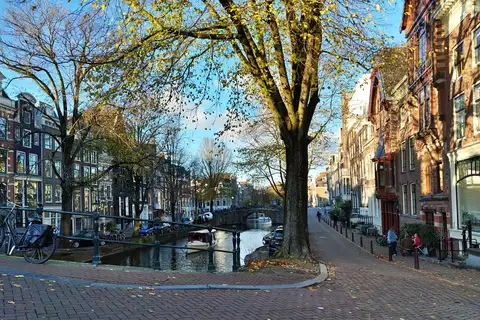 Canal de Ámsterdam en otoño con casas estrechas de ladrillo, barcos amarrados y bicicletas junto a un puente