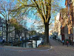 Canal de Ámsterdam en otoño con casas estrechas de ladrillo, barcos amarrados y bicicletas junto a un puente