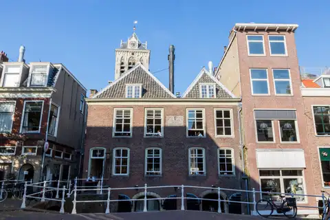 Casas históricas de ladrillo con frontones sobre un puente de barandilla blanca en Delft, con una torre al fondo