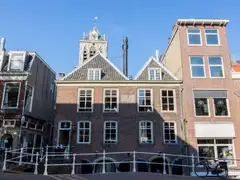 Casas históricas de ladrillo con frontones sobre un puente de barandilla blanca en Delft, con una torre al fondo