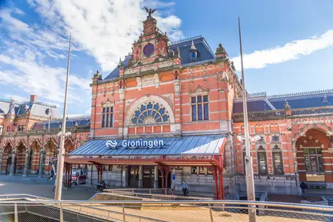 Fachada de ladrillo rojo de la histórica estación de Groninga con su marquesina y cielo azul con nubes