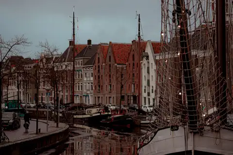 Barco de vela histórico amarrado en un canal de Groninga, con casas antiguas de ladrillo al fondo y reflejos
