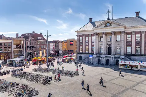 Grote Markt de Groninga con el ayuntamiento neoclásico, peatones y muchas bicicletas aparcadas en primer plano en un día soleado