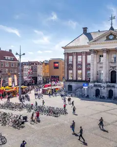 Grote Markt de Groninga con el ayuntamiento neoclásico, peatones y muchas bicicletas aparcadas en primer plano en un día soleado