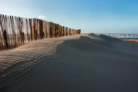 Dunas de arena con una valla de madera y la playa de Zandvoort aan Zee bajo un cielo claro, junto al mar del Norte
