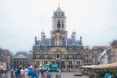 Ayuntamiento renacentista de Delft con su torre en la plaza del mercado, con terrazas, bicicletas y visitantes con impermeables
