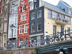 Bicicletas aparcadas a lo largo de un puente sobre un canal de Ámsterdam, con casas históricas de ladrillo estrechas al fondo