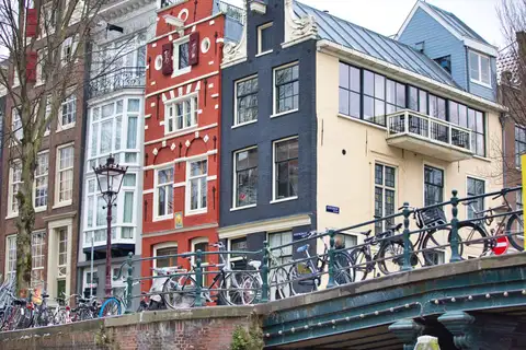 Bicicletas aparcadas a lo largo de un puente sobre un canal de Ámsterdam, con casas históricas de ladrillo estrechas al fondo