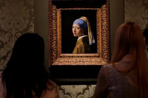 Dos visitantes de espaldas contemplan La joven de la perla de Vermeer en su marco dorado, en una sala del Mauritshuis