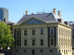 Fachada clasicista amarilla del Mauritshuis con frontón y tejado de pizarra, bajo un cielo azul despejado en La Haya