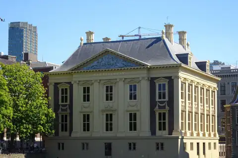 Fachada clasicista amarilla del Mauritshuis con frontón y tejado de pizarra, bajo un cielo azul despejado en La Haya