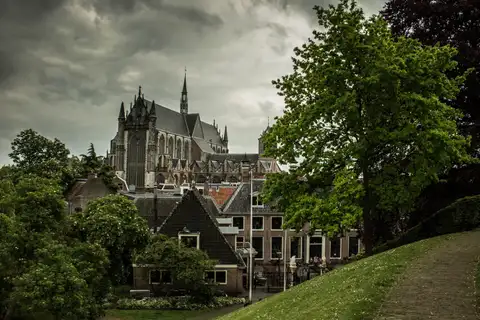 Iglesia gótica Hooglandse Kerk sobre los tejados de ladrillo del casco antiguo de Leiden, vista desde una colina de hierba con un camino empedrado