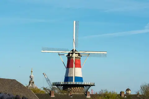 Molino De Valk de Leiden con la tela de los colores de la bandera neerlandesa, sobre los tejados de la ciudad y un cielo azul