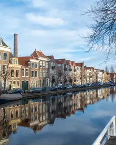 Canal de Leiden con casas de ladrillo del siglo XVII reflejadas en el agua, una chimenea de fábrica al fondo y un árbol sin hojas
