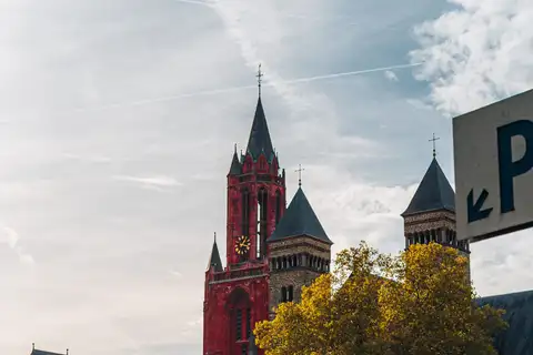 Torre roja de la iglesia de San Juan y las torres románicas de la basílica de San Servacio sobre los árboles otoñales del Vrijthof, Maastricht