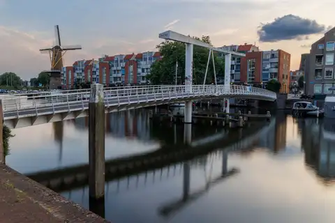 Puente levadizo blanco sobre el canal del puerto de Delfshaven al atardecer, con un molino de viento y edificios de ladrillo al fondo