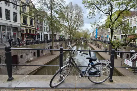 Bicicleta apoyada en la barandilla de un puente sobre el Oudegracht de Utrecht, con los muelles bajos y las casas a ambos lados