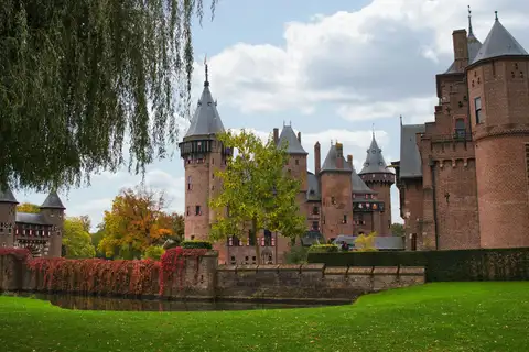 Castillo De Haar de ladrillo rojo con torres neogóticas, foso con hiedra otoñal y césped en primer plano, en Haarzuilens