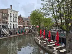 Terrazas con mesas y sombrillas rojas en los muelles junto al agua del Oudegracht de Utrecht, entre casas de ladrillo y árboles