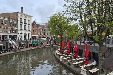 Terrazas con mesas y sombrillas rojas en los muelles junto al agua del Oudegracht de Utrecht, entre casas de ladrillo y árboles