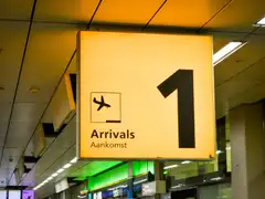 Cartel luminoso naranja de llegadas Arrivals / Aankomst con el número 1 y un avión en la terminal de un aeropuerto neerlandés