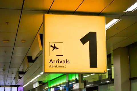 Cartel luminoso naranja de llegadas Arrivals / Aankomst con el número 1 y un avión en la terminal de un aeropuerto neerlandés