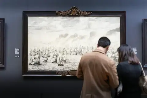 Dos visitantes de espaldas contemplan una gran marina del Siglo de Oro con batalla naval en una sala del Rijksmuseum