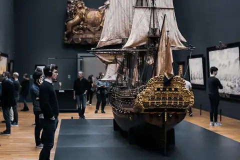 Maqueta de un navío de guerra del siglo XVII con velas y popa dorada, en una sala del Rijksmuseum con visitantes