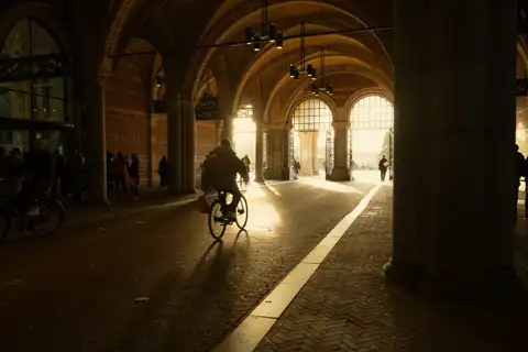 Ciclista cruzando el pasaje abovedado bajo el Rijksmuseum, con largas sombras sobre el pavimento de ladrillo