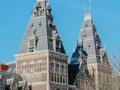Fachada de ladrillo rojo del Rijksmuseum con su torre y sus tejados de pizarra bajo un cielo azul despejado, en Ámsterdam