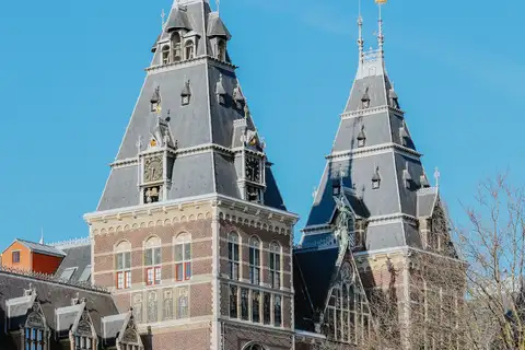 Fachada de ladrillo rojo del Rijksmuseum con su torre y sus tejados de pizarra bajo un cielo azul despejado, en Ámsterdam