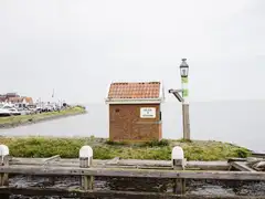 Entrada del puerto de Volendam con una caseta de ladrillo con el cartel Welkom in Volendam, el dique con casas y yates amarrados al fondo