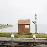 Entrada del puerto de Volendam con una caseta de ladrillo con el cartel Welkom in Volendam, el dique con casas y yates amarrados al fondo