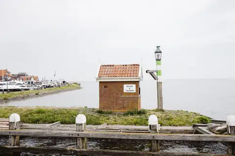 Entrada del puerto de Volendam con una caseta de ladrillo con el cartel Welkom in Volendam, el dique con casas y yates amarrados al fondo