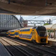Tren de dos pisos amarillo y azul de NS llegando a un andén de Amsterdam Centraal, con la antigua cubierta de la estación al fondo