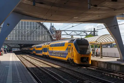 Tren de dos pisos amarillo y azul de NS llegando a un andén de Amsterdam Centraal, con la antigua cubierta de la estación al fondo