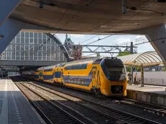 Tren de dos pisos amarillo y azul de NS llegando a un andén de Amsterdam Centraal, con la antigua cubierta de la estación al fondo