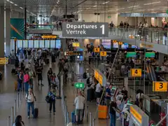Viajeros con maletas bajo el cartel Departures-Vertrek y los mostradores de facturación del aeropuerto de Ámsterdam-Schiphol