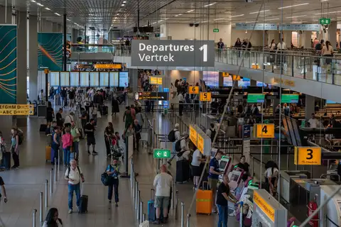 Viajeros con maletas bajo el cartel Departures-Vertrek y los mostradores de facturación del aeropuerto de Ámsterdam-Schiphol
