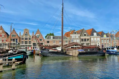 Barcazas tradicionales amarradas en el puerto de Hoorn frente a casas de ladrillo con gabletes escalonados, bajo un cielo azul