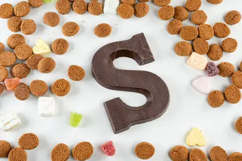 Letra S de chocolate negro rodeada de pepernoten, caramelos de colores y dulces en forma de corazón, típicos de Sinterklaas