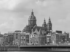 Fotografía en blanco y negro de la basílica de San Nicolás con sus torres y cúpula sobre casas y un puente de Ámsterdam