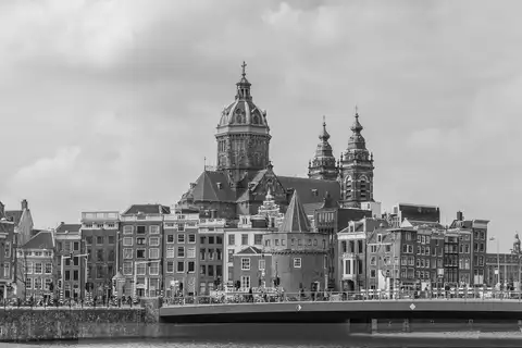 Fotografía en blanco y negro de la basílica de San Nicolás con sus torres y cúpula sobre casas y un puente de Ámsterdam