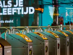 Hilera de barreras de acceso con lectores amarillos para tarjeta en una estación de metro de Ámsterdam, con carteles en neerlandés al fondo